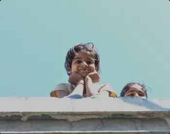 Two children smiling over a rooftop wall